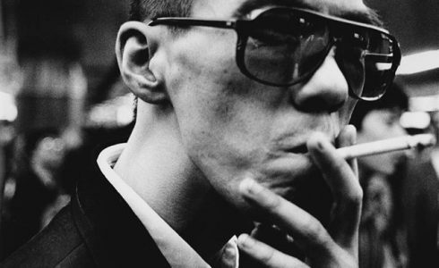 街头的一个吸烟男子。他的表情被巨大的眼睛框遮挡了。