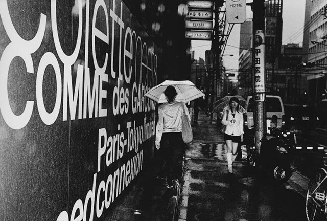 一个雨中的街头即景图：两个对面交汇的打伞的女子。